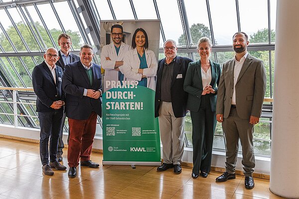 Gruppenfoto mit mehreren Personen, zwei davon abgebildet auf einem Roll-up-Display