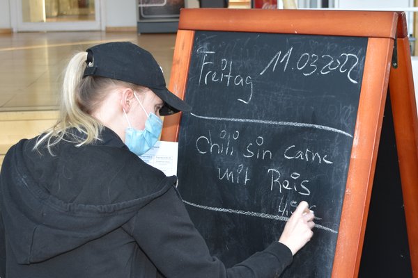Eine Frau schreibt das Tagesmenue auf eine Kreidetafel.