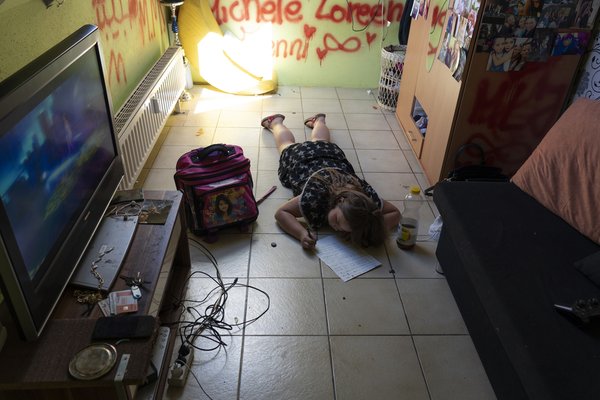 Foto: Kleines Mädchen beim Hausaufgaben machen auf dem Boden in ihrem verwahrlosten Zuhause. 