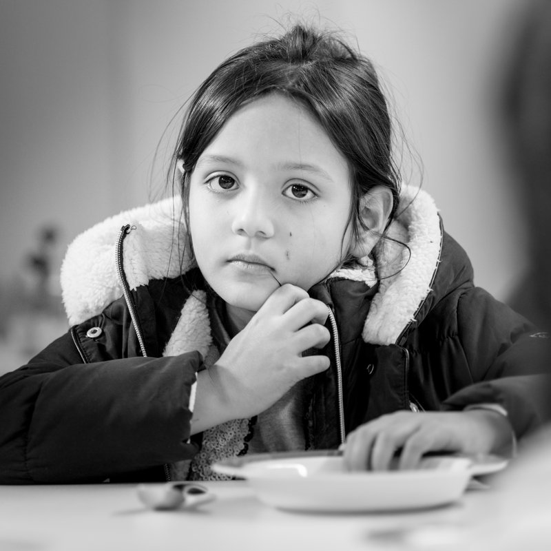 Foto: Schwarz-Weiß-Aufnahme eines kleinen Mädchens vor einem leeren Teller.